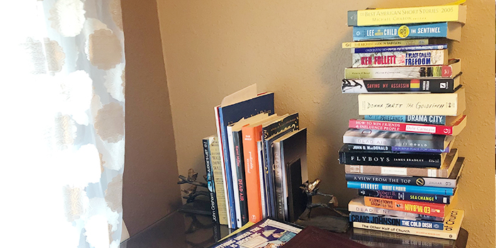 Many different books stacked on a side table