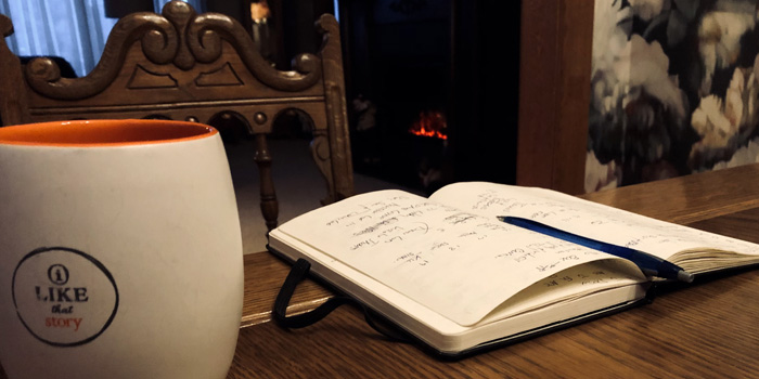 I Like That Story Mug sitting next to a journal with hand written notes on top of a wooden table